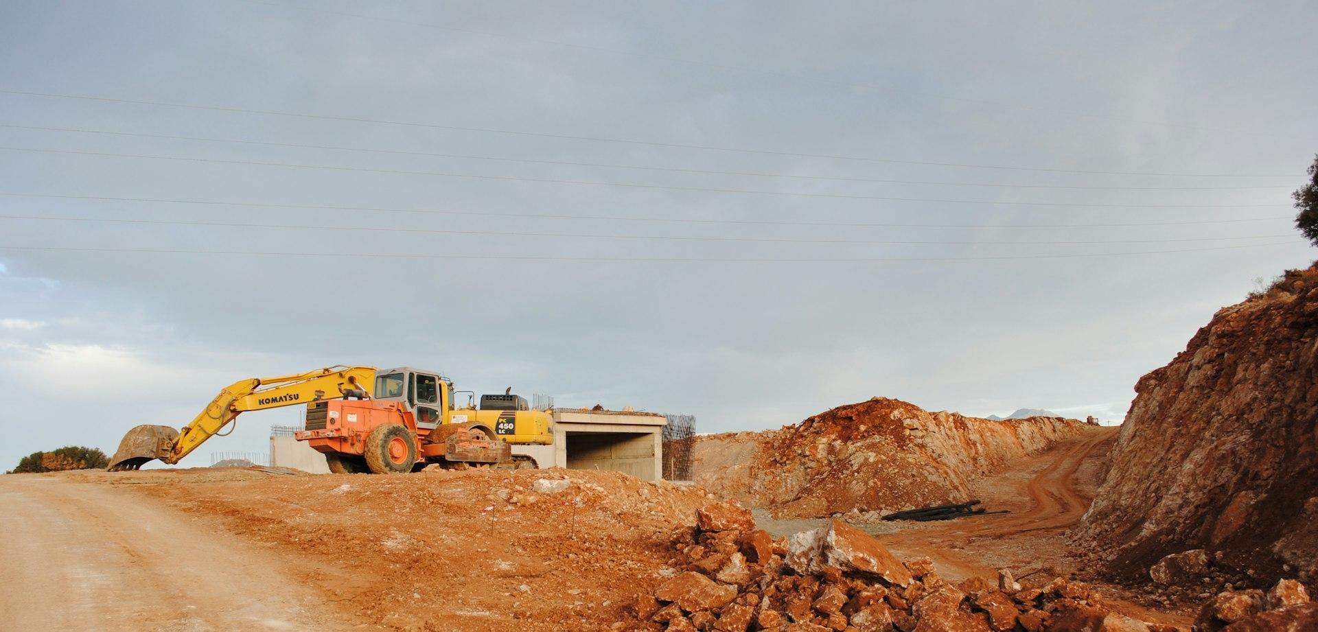yellow excavator near brown rock formation during daytime